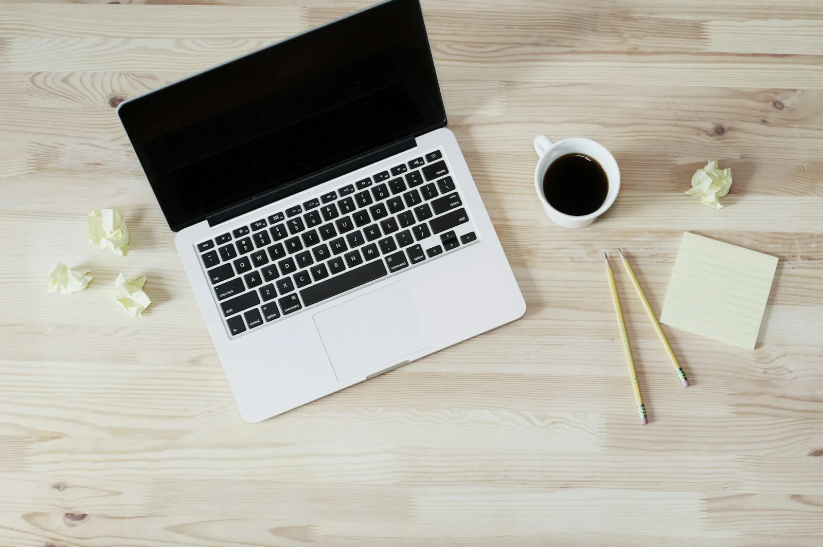 Image of a laptop, a coffee mug and some drafts on pieces of paper.